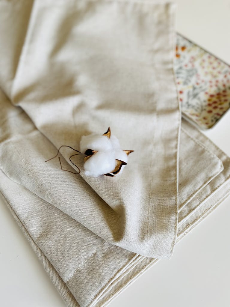 Close-up of a cotton boll resting on beige linen fabric. Neutral tones and soft texture.